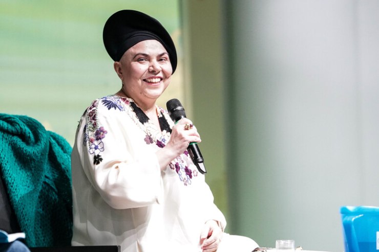foto della scrittrice Michela Murgia durante una conferenza con vestito bianco a fiori e cappello nero