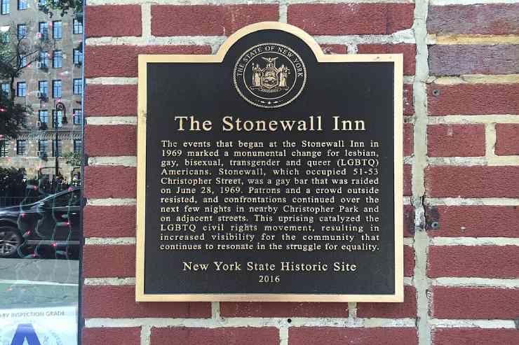 Placca nera commemorativa dei moti di Stonewall con scritte dorate su muro di mattoni 